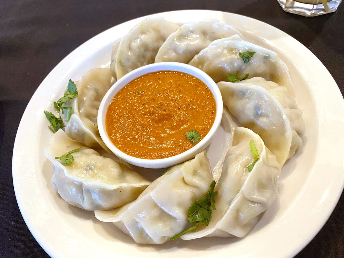Plate of momo dumplings with orange dipping sauce and cilantro – traditional Sherpa momo with spices in Scarborough